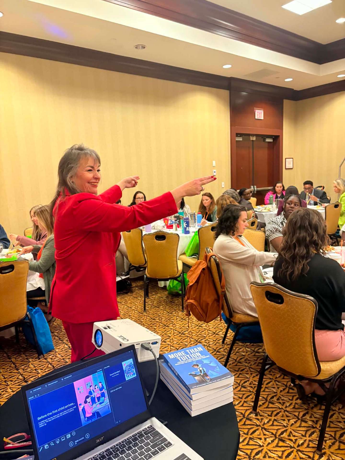 Kate Woodward Young in a red suit pointing toward audience members during a workshop